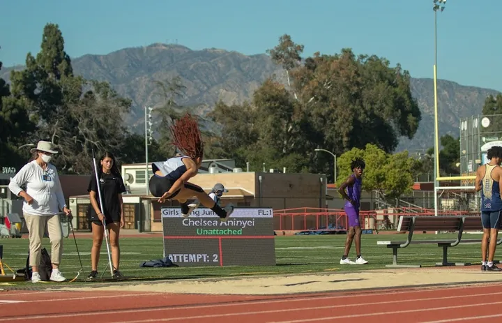 A long jumper in the air in front of a display board showing field event results